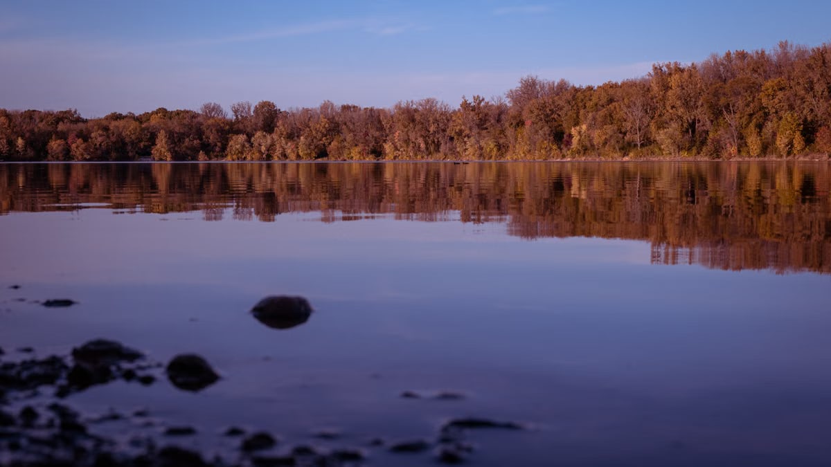 Tranquil view of a lake reflecting autumn trees under a blue sky.